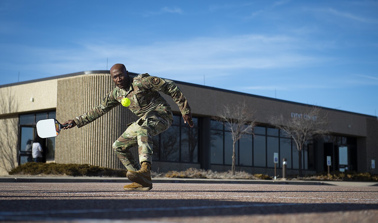 Player lunging to hit a pickleball on a parking lot outside an event center building